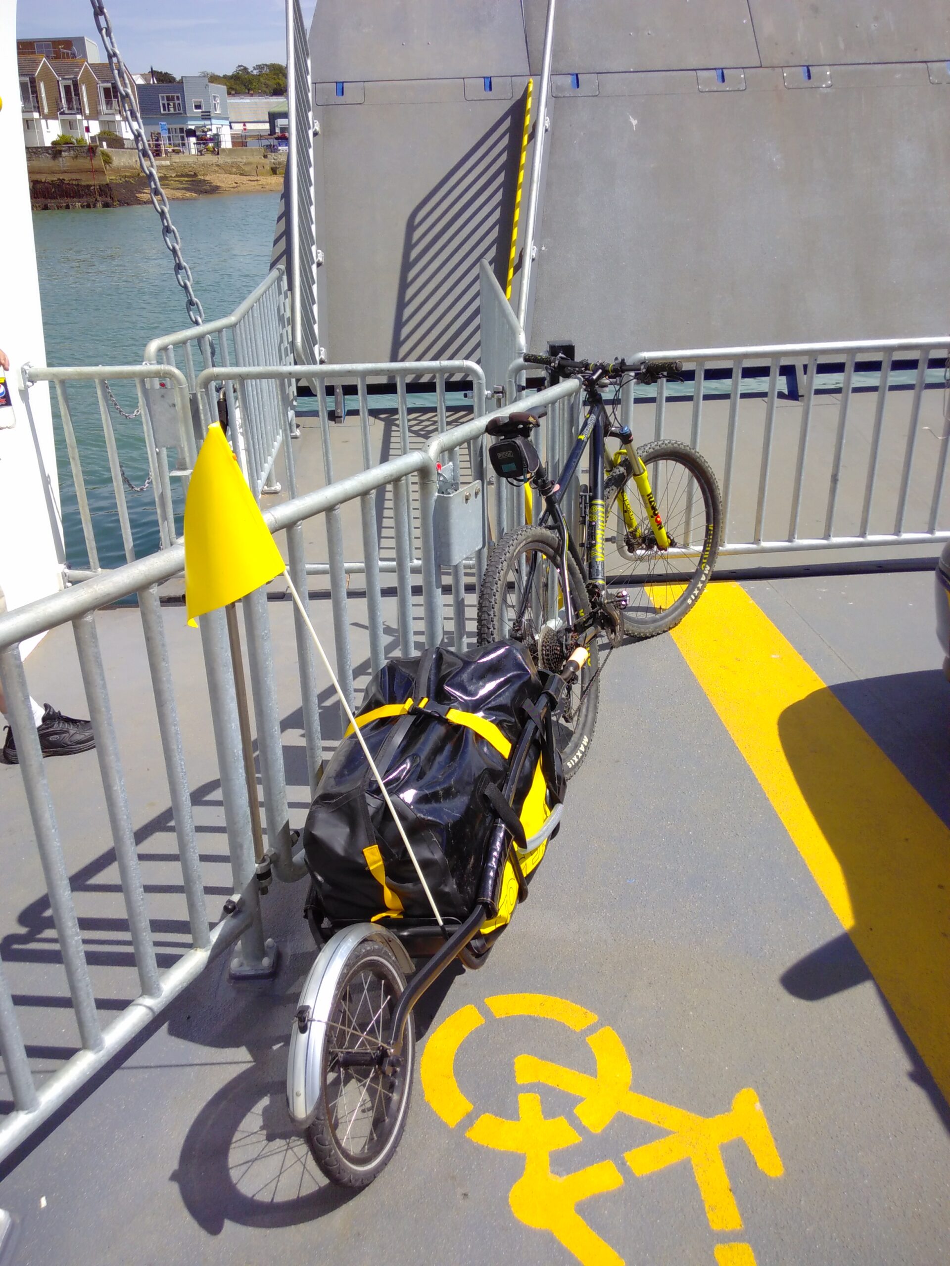 Abicycle with a trailer attached leans on railings aboard a small ferry.