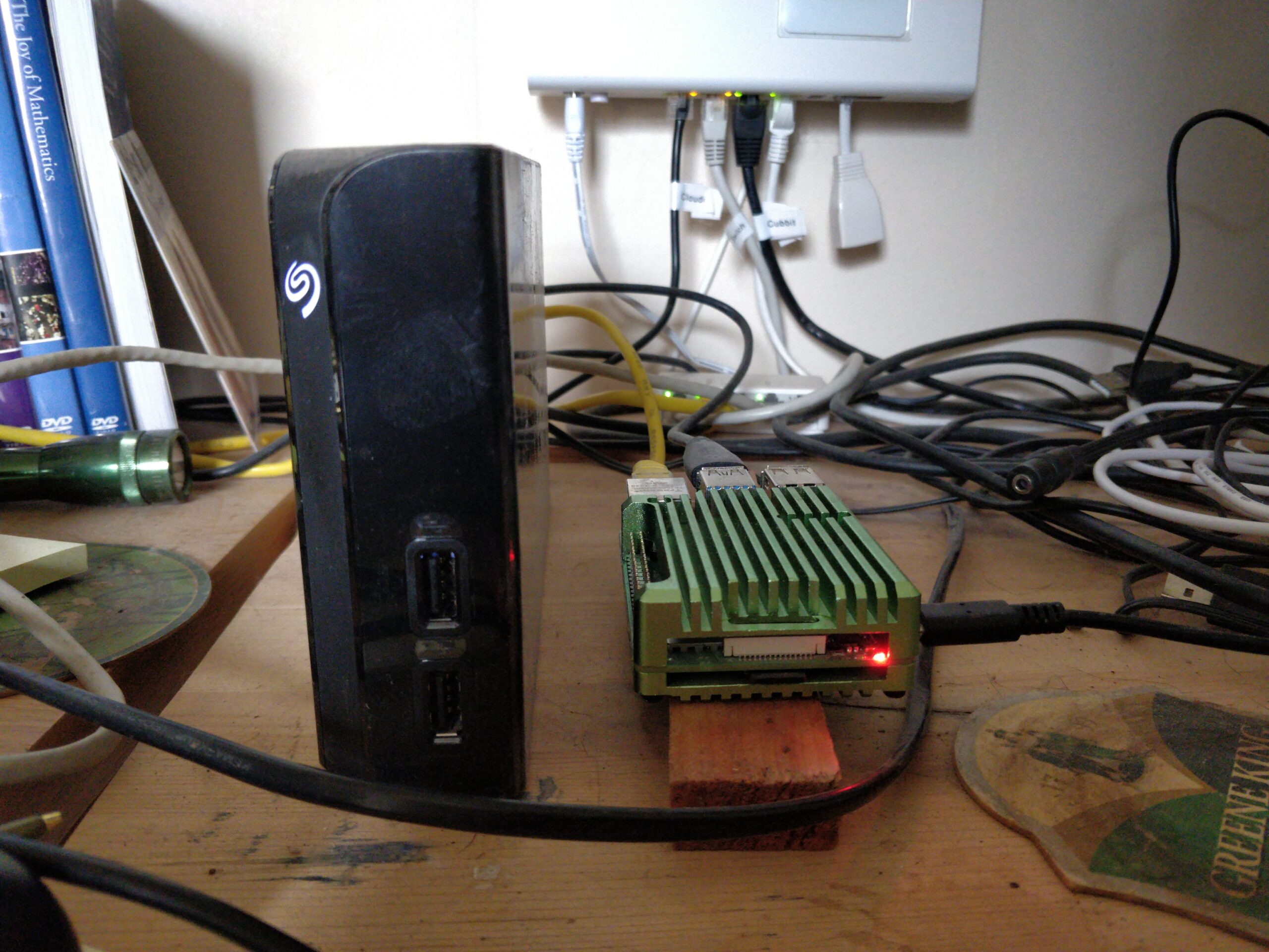 An external hard drive case looms over the Raspberry Pi case to which it is attached. A confusion of wires sits behind them.
