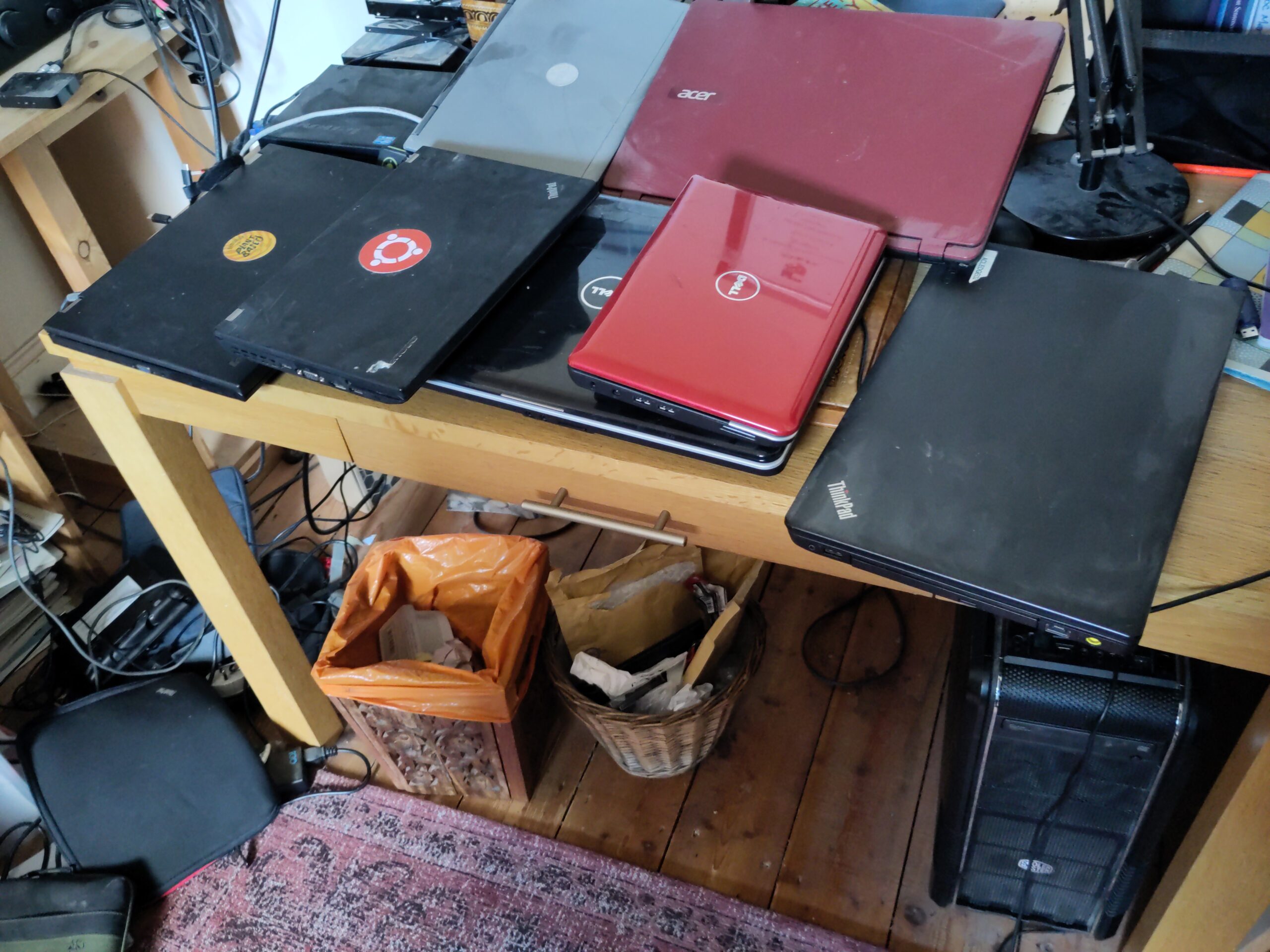 A variety of laptop computers sit on an untidy desk, and a large computer case sits beneath it.