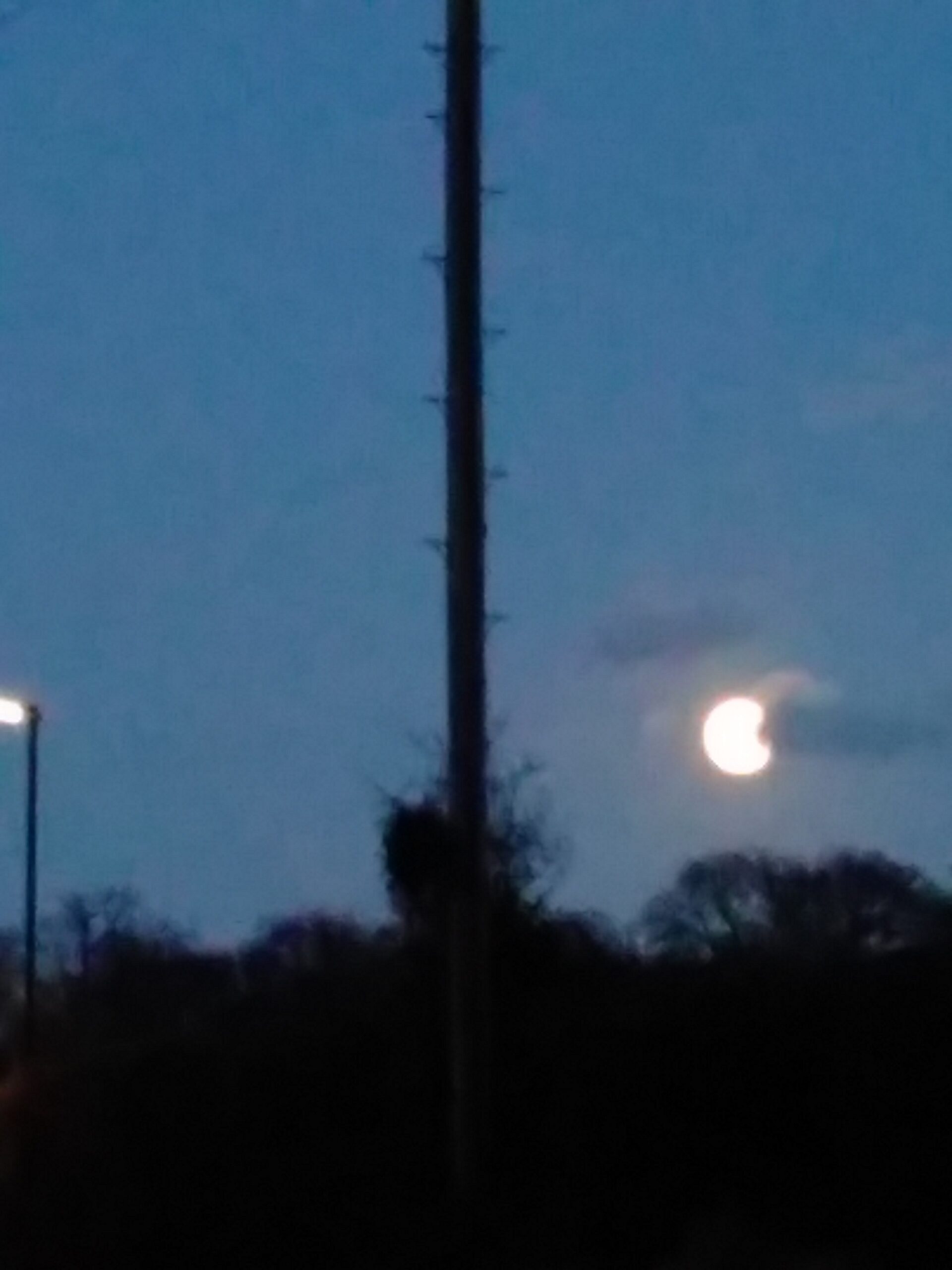 A picture of the moon in the dark evening sky, with a cloud just cutting into its edge.