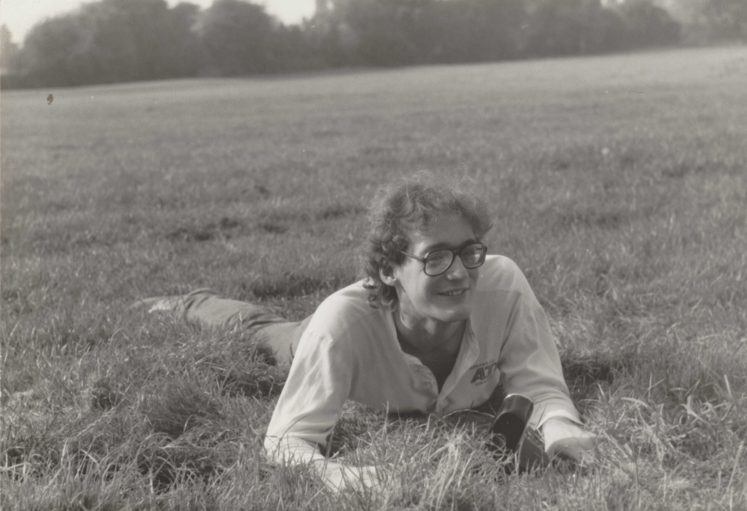 A black-and-white image of a teenage boy with long hair and glasses, grinning at the camera